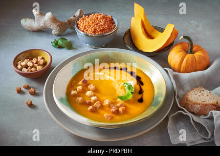 Crème de lentilles rouges et de Citrouille en soupière et Bol en céramique assaisonnée de basilic, crème et croûtons. Tranches de citrouille, les lentilles, le gingembre et l'assaisonnement autour Banque D'Images