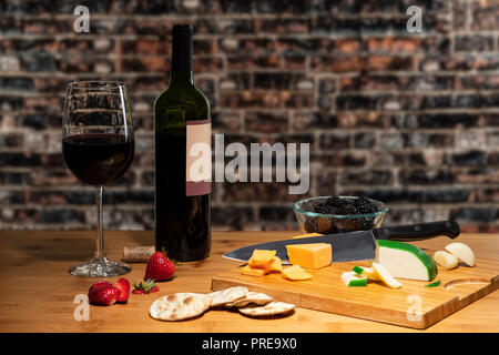 Et un verre de vin accompagné de fromage sur une table avec une planche à découper et couverts de fruits. Banque D'Images