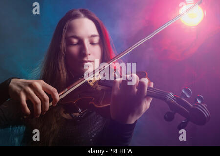 Belle fille à jouer du violon. Brouillard multicolores à l'arrière-plan. Studio shot Banque D'Images