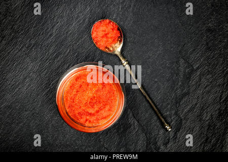 Une photo prise à la verticale de caviar rouge dans un bocal et dans une cuillère, tourné à partir de ci-dessus, sur un fond noir avec une place pour le texte Banque D'Images