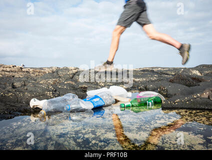 Low angle view of jogger passé en courant les bouteilles en plastique dans la région côtière de rockpool, plage Banque D'Images