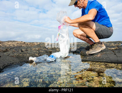 Un Plogger/jogger recueille des ordures en plastique de la plage rockpool durant son jogging Banque D'Images