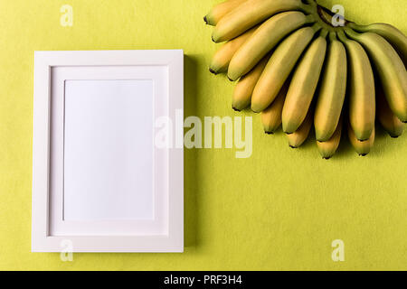 Style minimaliste. Cadre photo blanc vide et la banane fruit contre résumé du papier de couleur, copie d'arrière-plan, l'espace de mise à plat. Banque D'Images