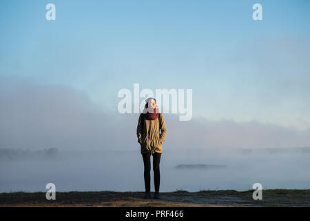 Femme se tient dans la lumière du soleil du matin en face de la belle nature paysage couvert de brouillard. Female hiker profitant soleil levant dans misty natural background Banque D'Images