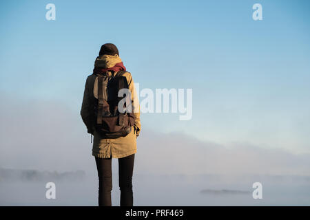 Femme se tient dans la lumière du soleil du matin en face de la belle nature paysage couvert de brouillard. Female hiker profitant soleil levant dans misty natural background Banque D'Images