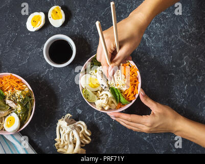 Les mains des femmes. Le miso Ramen nouilles asiatiques dans des bols en pierre sombre arrière-plan. Vue d'en haut Banque D'Images