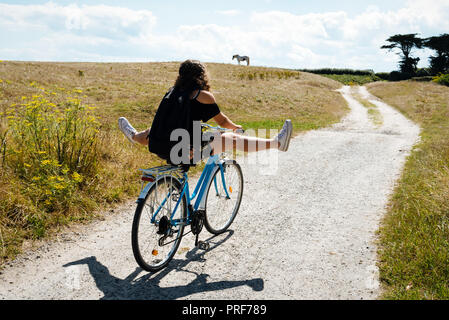 Pretty young woman riding bicycle in a country road avec ses jambes en l'air Banque D'Images