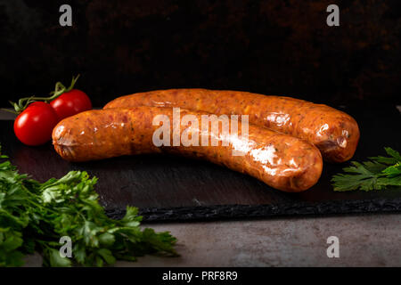 Deux saucisses de porc fumé avec des herbes et des tomates de sherry sur une ardoise foncé Banque D'Images