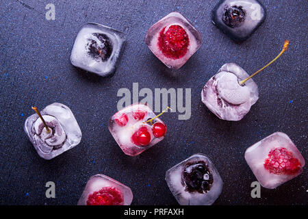 Petits fruits congelés (framboises, mûres, myrtilles, groseille, cerise) dans ice cube sur tissu blanc arrière-plan. Vue d'en haut. Banque D'Images