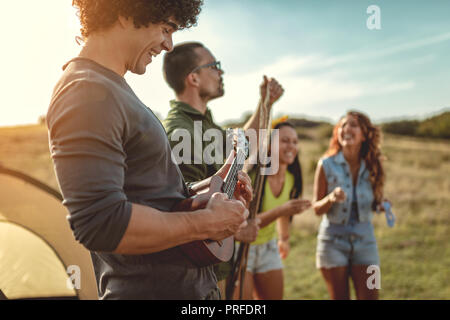 Les jeunes ont un bon temps au camp dans la nature. Ils se reposer, rire et chanter avec la musique d'ukulélé, heureux d'être ensemble. Banque D'Images