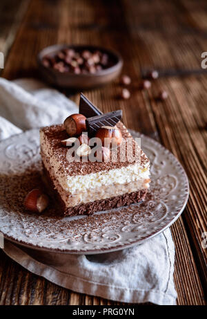 Délicieux gâteau au chocolat avec crème fouettée et noisettes, garni de couches de poudre de cacao Banque D'Images