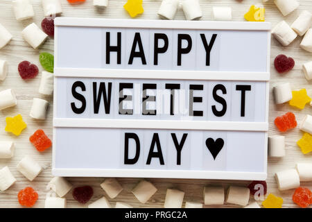 Conseil moderne avec texte 'Happy Sweetest Day' mot et candy sur la surface en bois blanc, vue du dessus. À partir de ci-dessus, mise à plat, les frais généraux. Banque D'Images