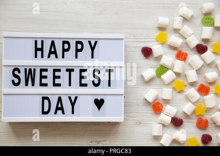 Conseil moderne avec texte 'Happy Sweetest Day' mot et candy sur la surface en bois blanc, vue de dessus. Vue de dessus, des laïcs, des frais généraux. Banque D'Images