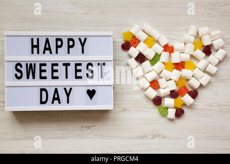 Conseil moderne avec texte 'Happy Sweetest Day' mot et coeur en bonbons blanc sur fond de bois, vue du dessus. À partir de ci-dessus, mise à plat, les frais généraux. Banque D'Images