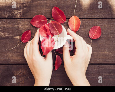 Belle, feuilles rouges, Women's Hands, tasse de café fort et Brown, vintage, surface en bois. Vue de dessus, close-up Banque D'Images