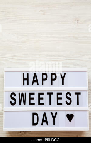 Conseil moderne avec texte 'Happy Sweetest Day' mot over white surface en bois, vue du dessus. À partir de ci-dessus, mise à plat, les frais généraux. Copier l'espace. Banque D'Images