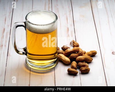 Chope de bière légère avec des cacahuètes sur la table en bois clair Banque D'Images