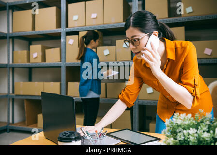 Manager dans l'e-boutique société est client appelant pour confirmer les marchandises qu'ils ont commandées, et les autres membres du personnel est de compter les marchandises dans l'arrière-plan Banque D'Images