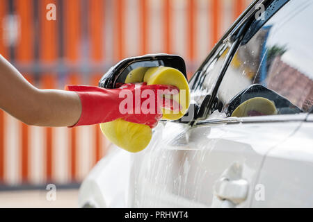 Hand holding sponge lave-miroirs latéraux d'une voiture Banque D'Images