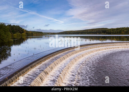 L'eau s'écoule plus de déversoir pittoresque calme lac bordé d'arbres, sous ciel bleu profond - Réservoir d'Fewston, Washburn Valley, North Yorkshire, Angleterre, Royaume-Uni.