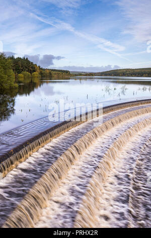 L'eau s'écoule plus de déversoir pittoresque calme lac bordé d'arbres, sous ciel bleu profond - Réservoir d'Fewston, Washburn Valley, North Yorkshire, Angleterre, Royaume-Uni.