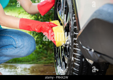 Femme tenant un lave-éponge les roues de sa voiture Banque D'Images
