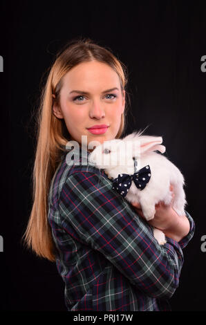 Belle fille blonde wearing plaid shirt, holding lapin blanc avec ruban en pointillés Banque D'Images