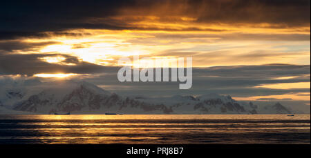 La lumière au coucher du soleil à travers les nuages au-dessus des montagnes enneigées, Péninsule Antarctique Banque D'Images