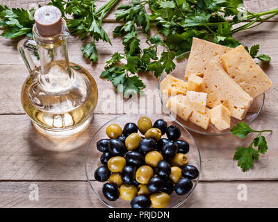 Olives, olives sur une plaque de verre, de l'huile végétale dans un pot, le fromage, le persil sur un fond de bois Banque D'Images