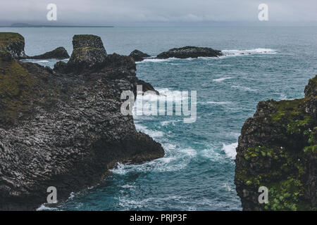 Vue panoramique des falaises moussues en face de l'océan bleu à Arnarstapi, Islande le jour nuageux Banque D'Images