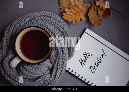 Feuilles d'automne jaune et orange, une tasse de thé enveloppé dans une écharpe en tricot chaud et bloc-notes avec poignée sur fond gris, vue d'en haut Banque D'Images