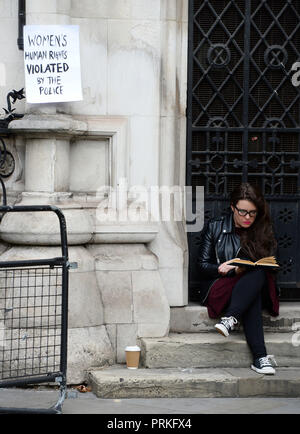 Une femme lit un livre à côté d'un signe de protestation à l'extérieur de la Royal Courts of Justice, Londres, où les pouvoirs d'un tribunal est saisi de l'affaire de Kate Wilson qui a été trompé dans une relation par l'agent d'infiltration Mark Kennedy. Banque D'Images