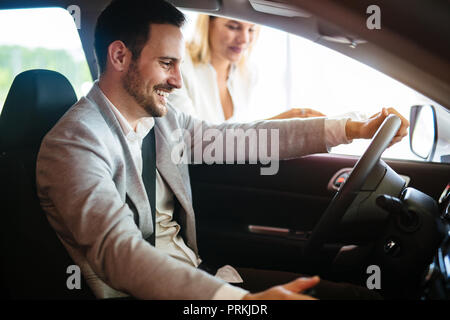 Portrait de beau jeune homme en prenant à la voiture de luxe pour test drive, assis à l'intérieur et souriant Banque D'Images