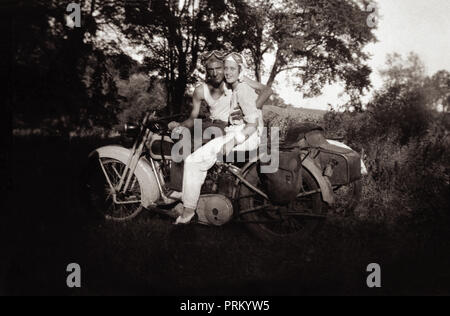 Jeune homme & amie portant des casques et lunettes assis sur leur Harley Davidson 1948 1000cc 'crétin' & moto side-car à la campagne en Banque D'Images