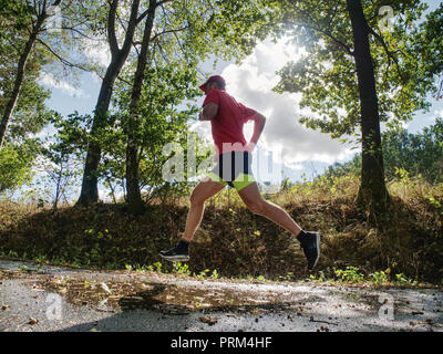 Coureur de l'homme pantalon short noir jaune et rouge t-shirt saute sur la piscine sur route asphaltée. Soirée fitnes exercice dans le parc automne Banque D'Images