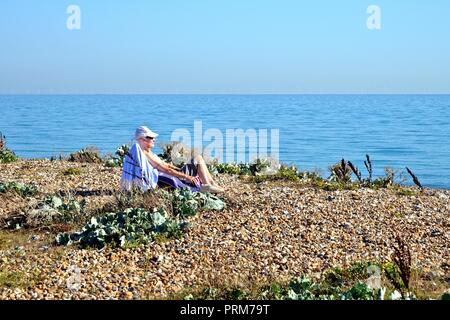 Vieille Femme assis sur une chaise en train de bronzer sur la plage de Littlehampton West Sussex England UK Banque D'Images