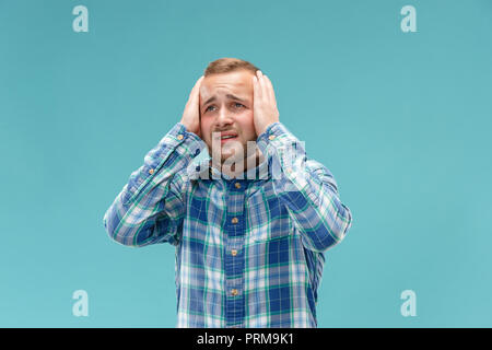 Horrible, stress, choc. Portrait de mi-longueur mâle isolée au studio bleu. Jeune homme malheureux émotionnelle qui serre la tête dans les mains. Les émotions humaines, l'expression faciale concept. Couleurs tendance Banque D'Images