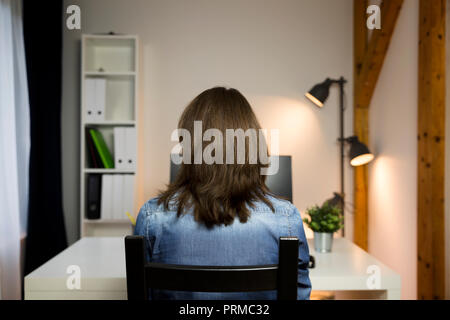 Femme assise à la table de travail à côté de l'ordinateur. Travail tard la notion Banque D'Images