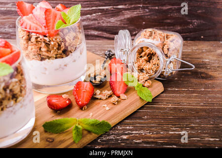 Dans les verres parfait au yogourt avec granola, les fraises et les feuilles de menthe. Sur planche de bois. Petit-déjeuner sain concept. Table en bois rustique, d'arrière-plan. Banque D'Images