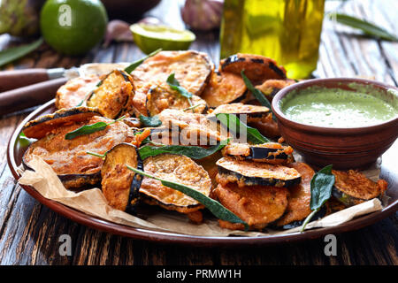 Aubergine Aubergine frit pané tranches sur une plaque de faïence avec du yaourt persil trempant dans un bol d'argile sur une table rustique avec des ingrédients à l'arrière Banque D'Images