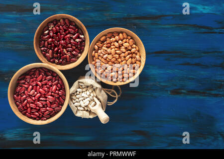 Assortiment de plats en bois dans les haricots et les haricots blancs dans un sac de lin bleu foncé sur fond de bois, de haricot mungo, haricot rouge, haricot blanc Banque D'Images