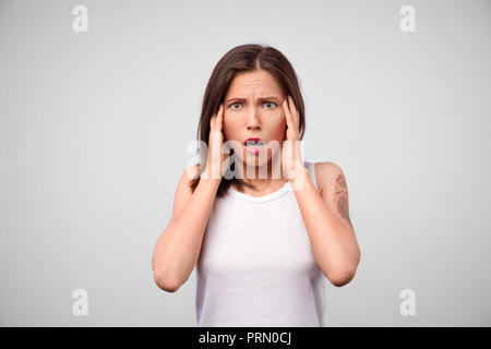 Horrible, stress, choc. Moitié femelle portrait en pied isolé à gray studio. Jeune femme surprise émotionnelle qui serre la tête dans les mains. Les émotions humaines, Banque D'Images