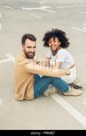 Happy young couple interracial smiling at camera while sitting on street Banque D'Images