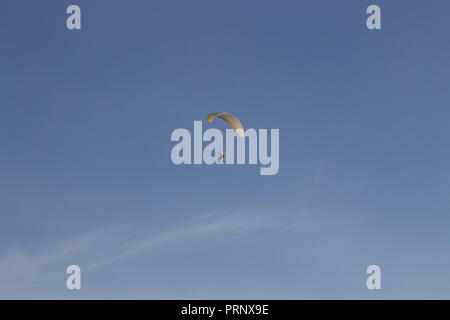 Seul Powered parapentiste avec auvent rouge et jaune dans le ciel bleu et les nuages vaporeux Banque D'Images