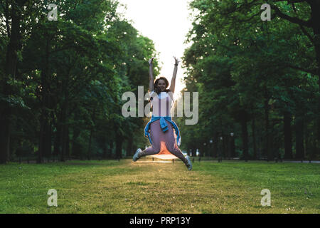 Jeune femme sautant avec large arms on meadow in park Banque D'Images