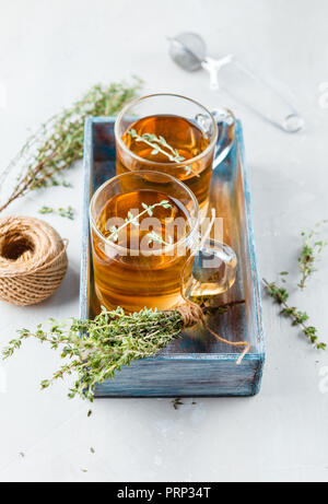 Verre transparent tasse de tisane au thym et branches de thym attachés en tas dans boîte en bois bleu sur fond blanc Banque D'Images