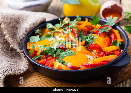Shakshuka, œufs frits cuits dans la sauce tomate et les poivrons dans la poêle en fonte sur table en bois rustique Banque D'Images