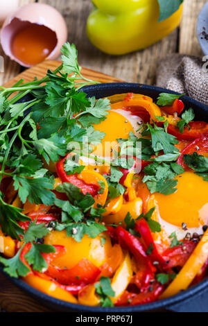 Shakshuka, œufs frits cuits dans la sauce tomate et les poivrons dans la poêle en fonte sur table en bois rustique Banque D'Images