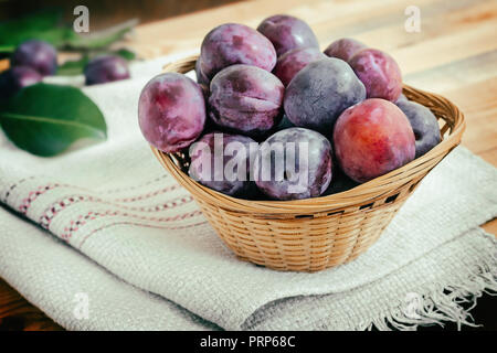 Sur la table sur une serviette panier en osier rempli de grosses prunes mûres. Banque D'Images