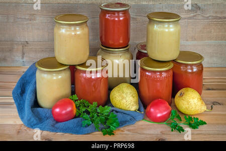 Purée de poire et le jus de tomate sont conservés dans des bocaux en verre avec couvercles métalliques scellés. Près de se coucher les poires et les tomates. Banque D'Images